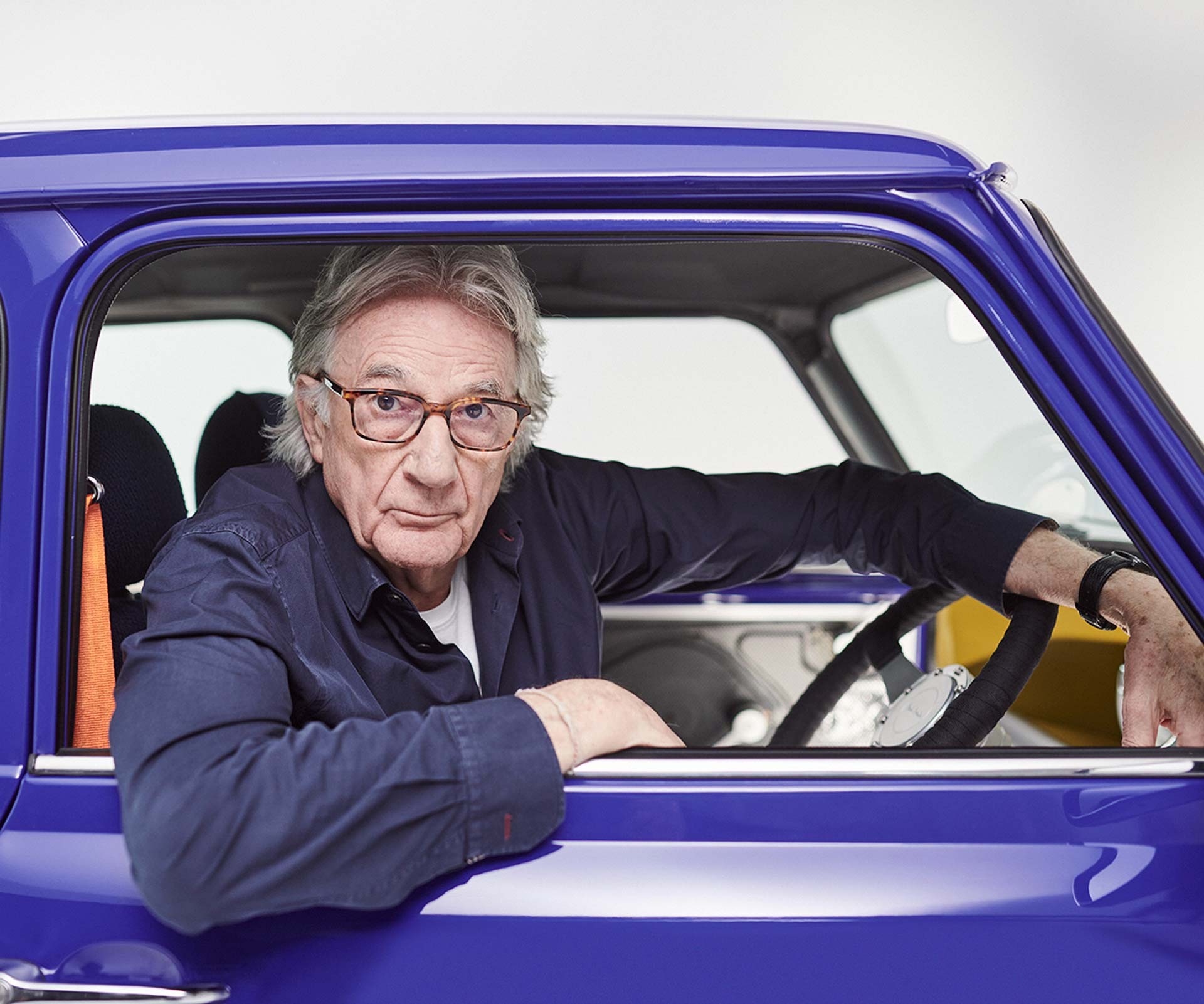 Paul Smith in his MINI Recharged, looking out of the window into the camera. An elbow hangs loosely over the lowered window.